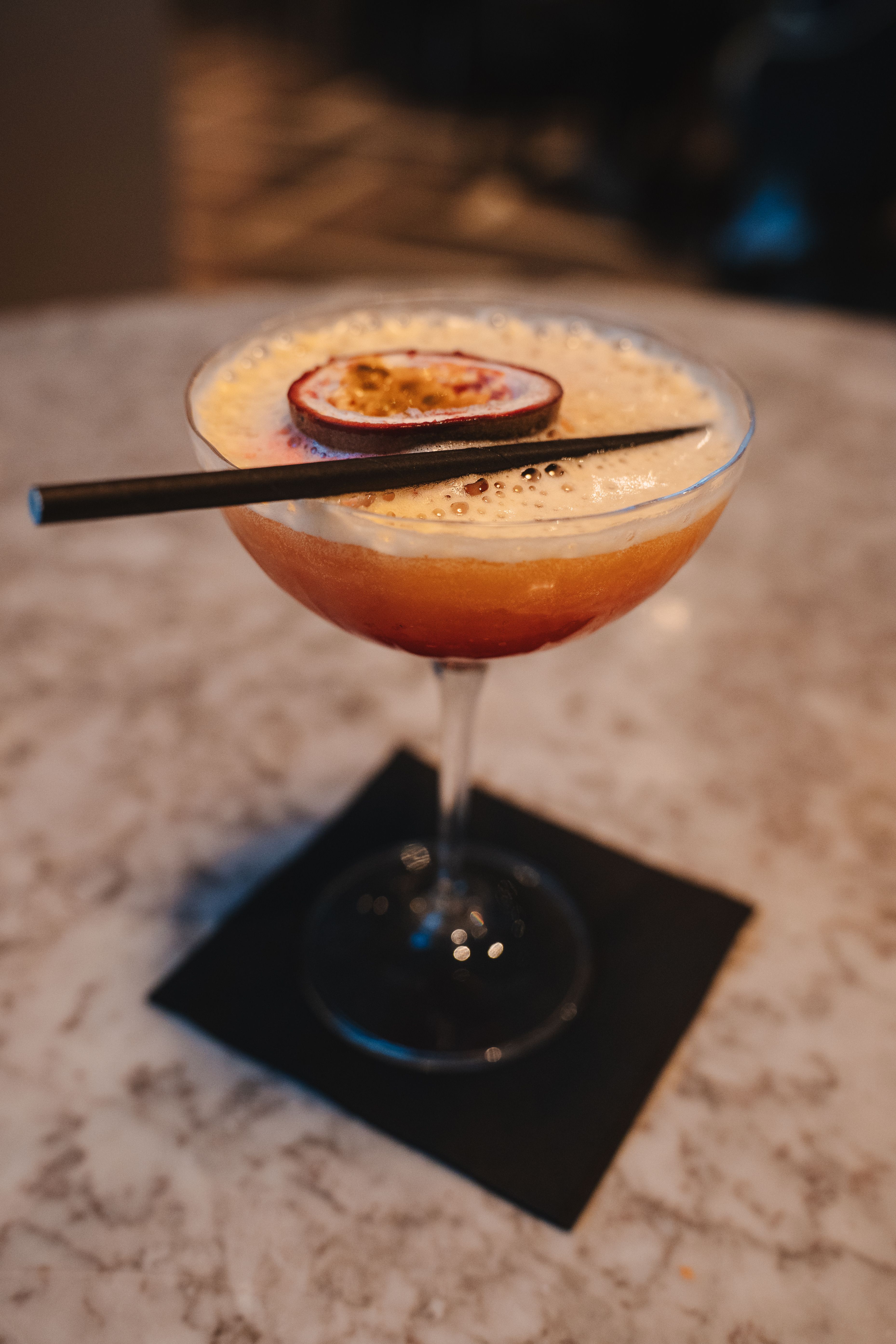 A coupe cocktail with passion fruit garnish on a marble bar.